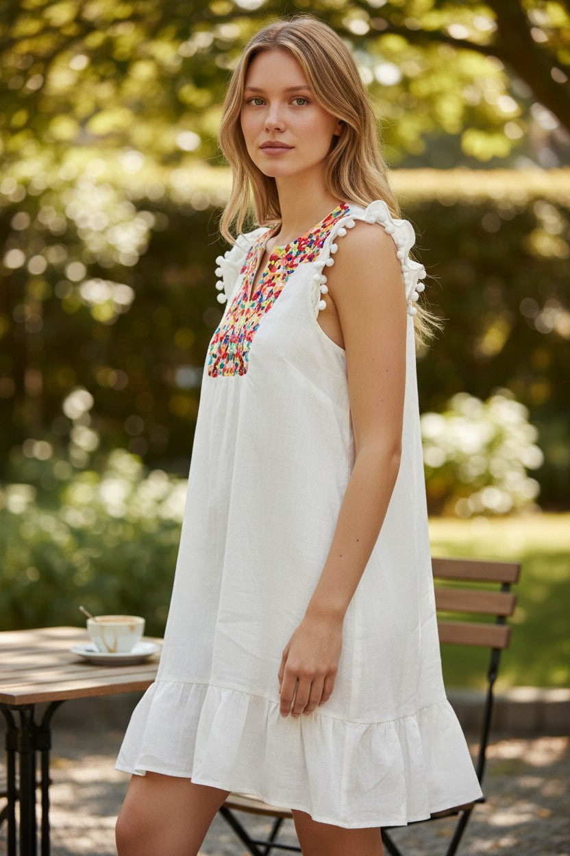 Lady Bear Resale white linen dress with colorful embroidered V-neck, pom-pom trim on flutter sleeves and ruffled hem.